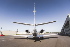 Rear view of Cessna Citation XLS+ N975MD parked on the tarmac outside an aircraft hangar. The image shows the jet’s twin engines, tail assembly, and horizontal stabilizers under clear blue skies, highlighting the aircraft’s sleek aerodynamic design.